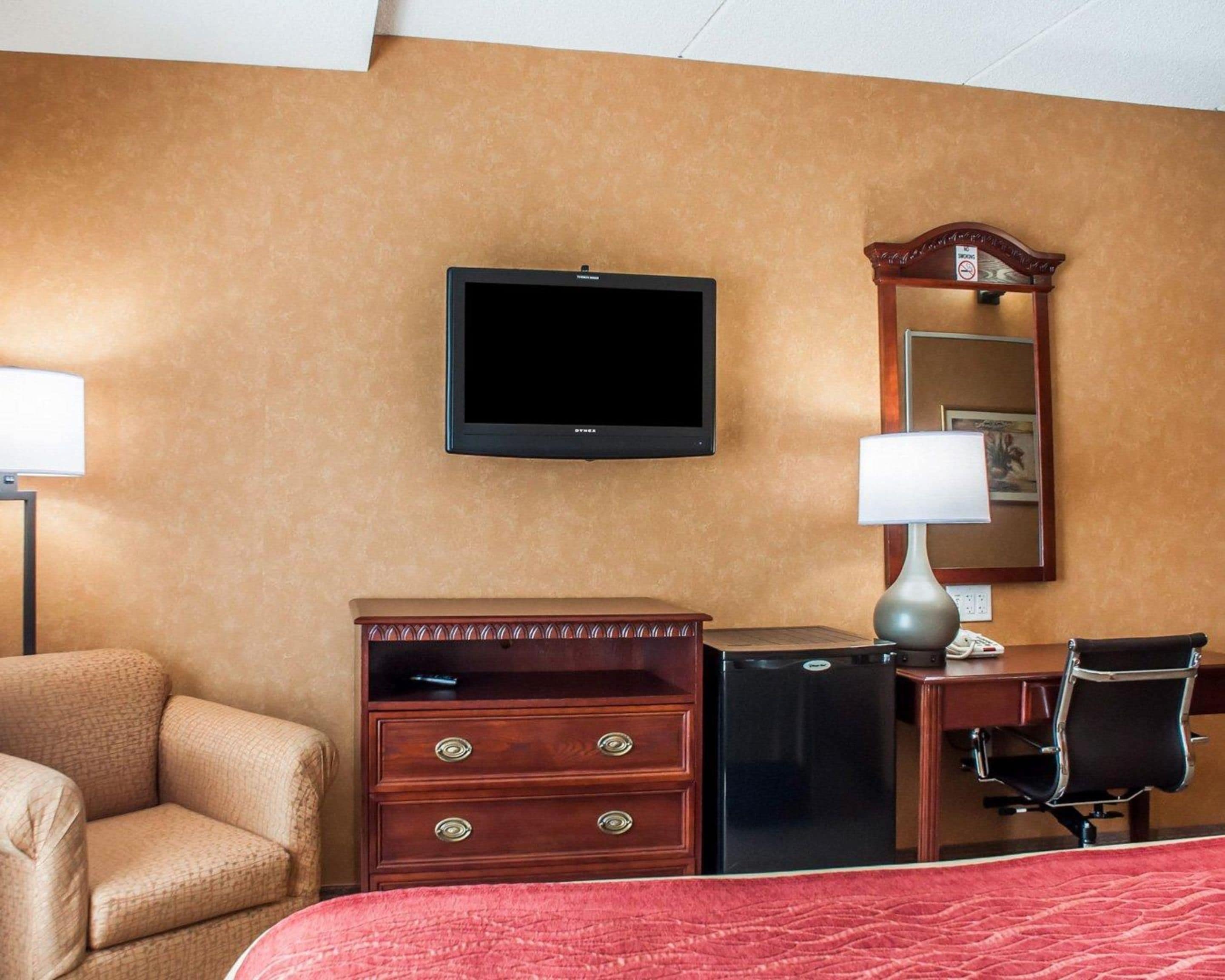 Een hotelkamer met een bed, een bureau met stoel, een dressoir, een televisietoestel en een spiegel.