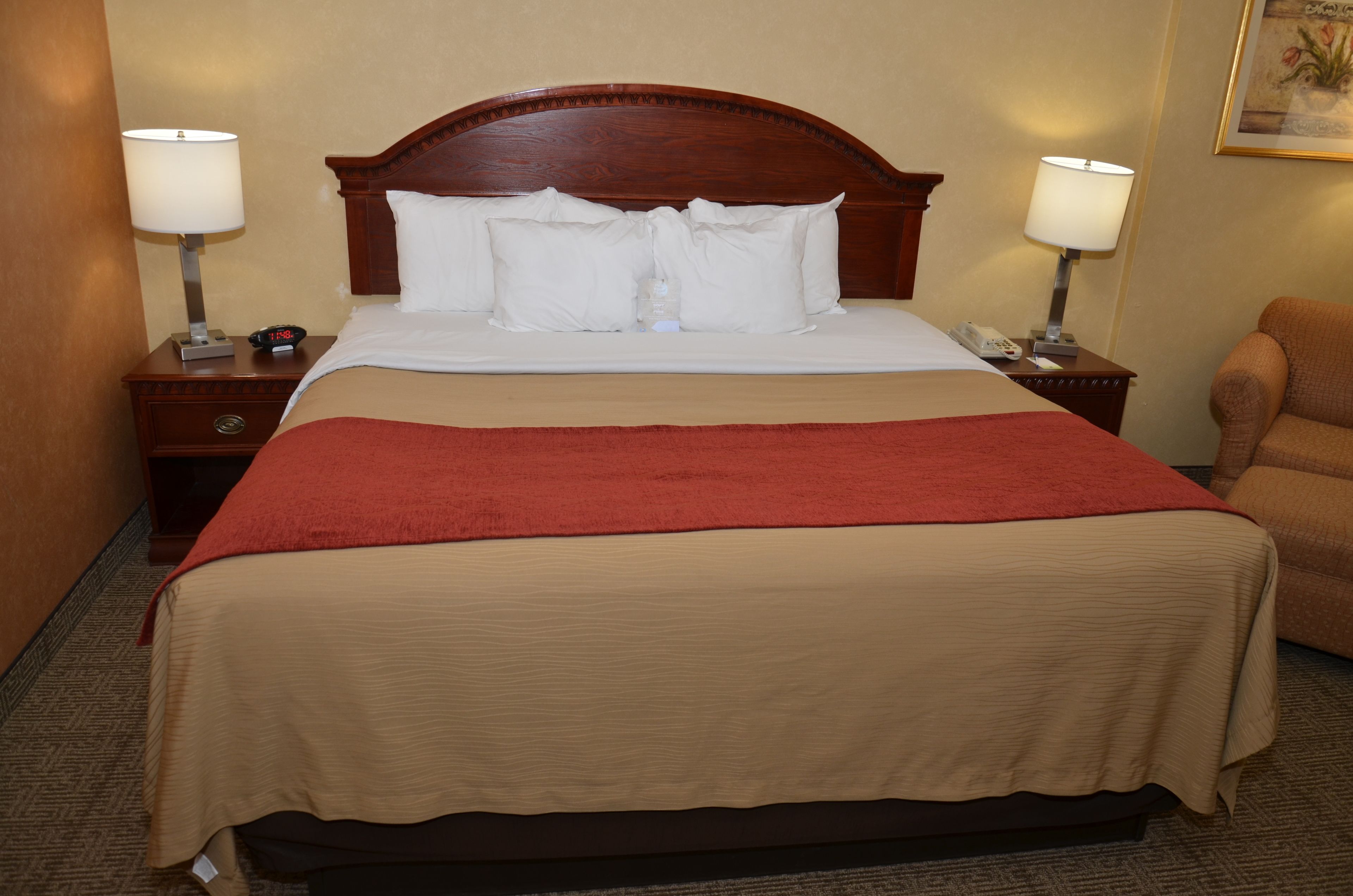 A hotel room with a large bed, two bedside tables, a red throw blanket, and a chair.