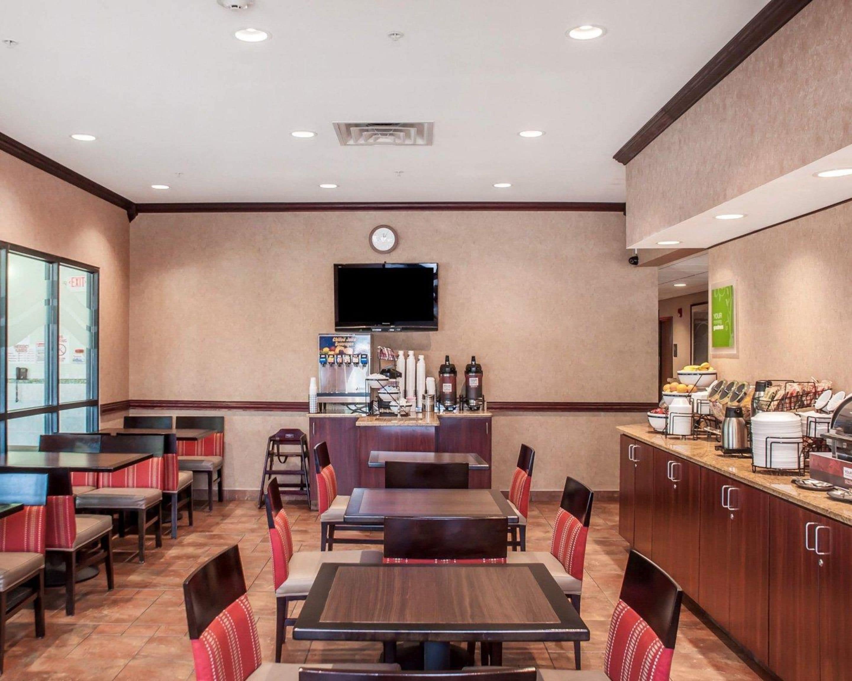 A hotel dining area with tables and chairs, a coffee station, and a TV mounted on the wall.