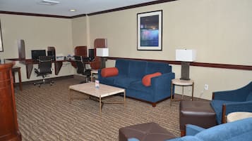 A hotel room with a blue sofa, a wooden desk, a computer, and a framed picture on the wall.