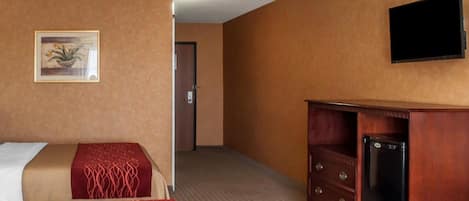 Una habitación de hotel con una cama, un aparador, un televisor y una puerta que da a otra habitación.