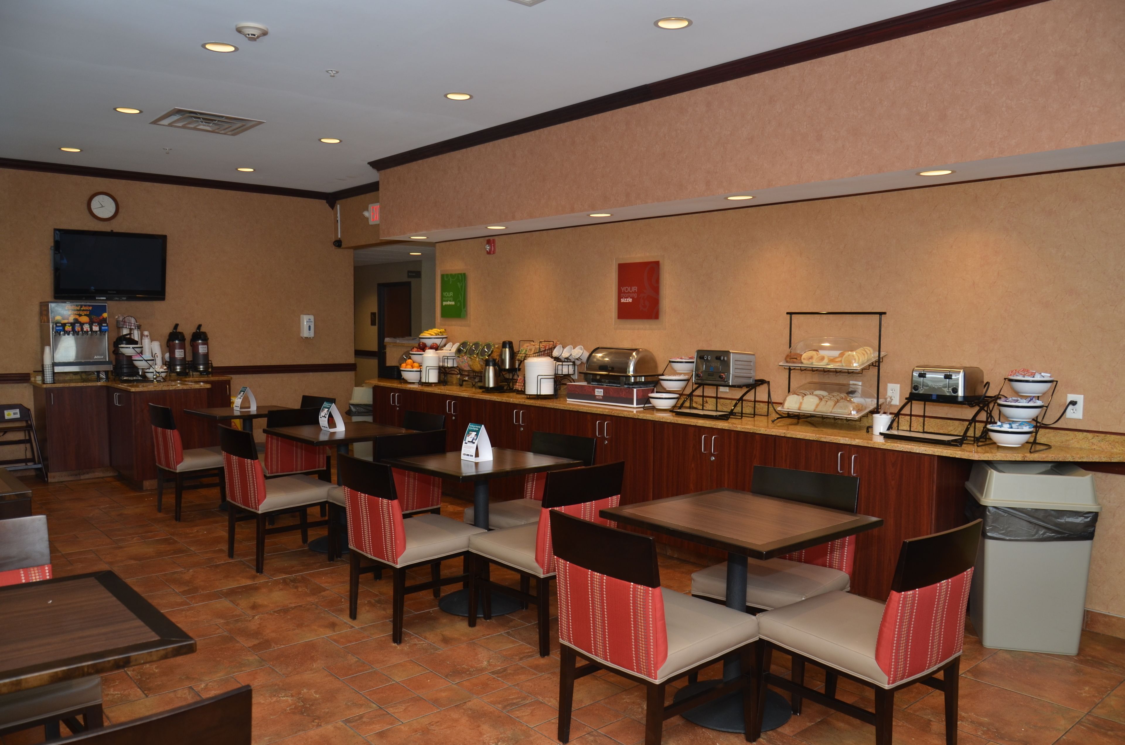 A hotel breakfast area with tables, chairs, a coffee station, and a trash bin.