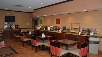 A hotel breakfast area with tables, chairs, a coffee station, and a trash bin.