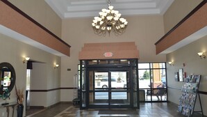 A hotel lobby with a revolving door, a chandelier, a reception desk, and a magazine rack.