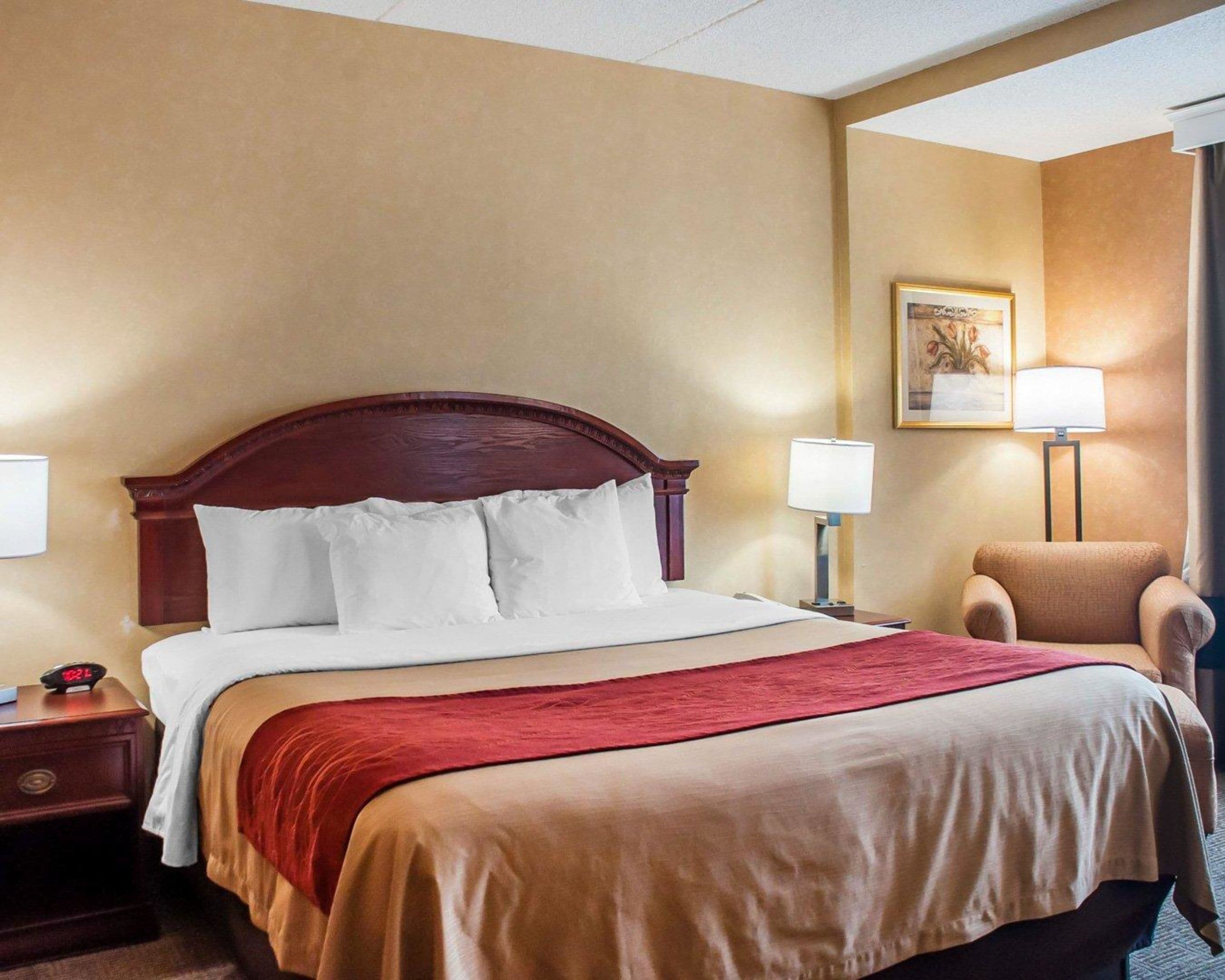 A hotel room with a large bed, two bedside tables, a chair, and a painting on the wall.
