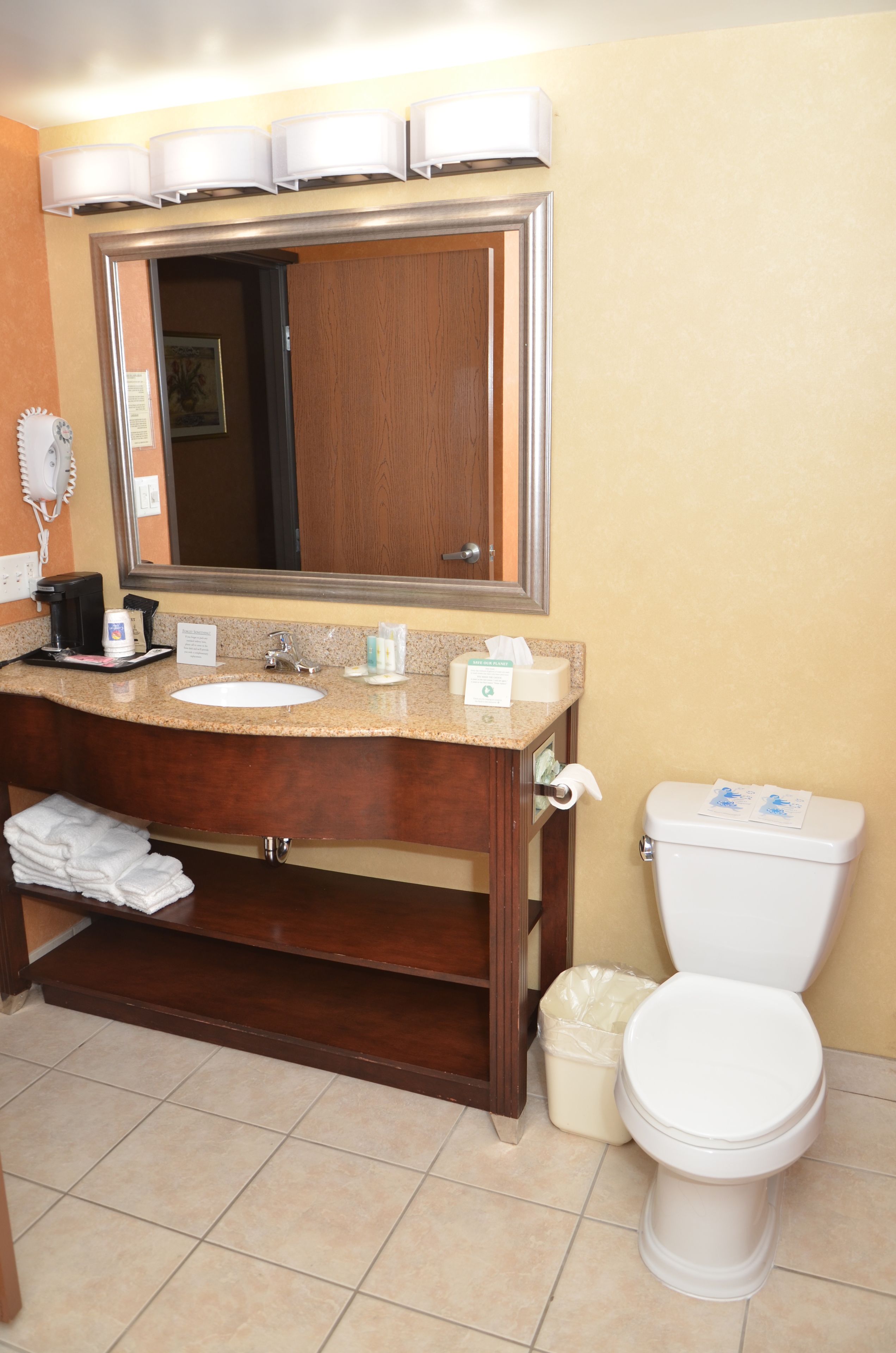 A bathroom with a wooden vanity, a sink, a mirror, a toilet, and a trash can.