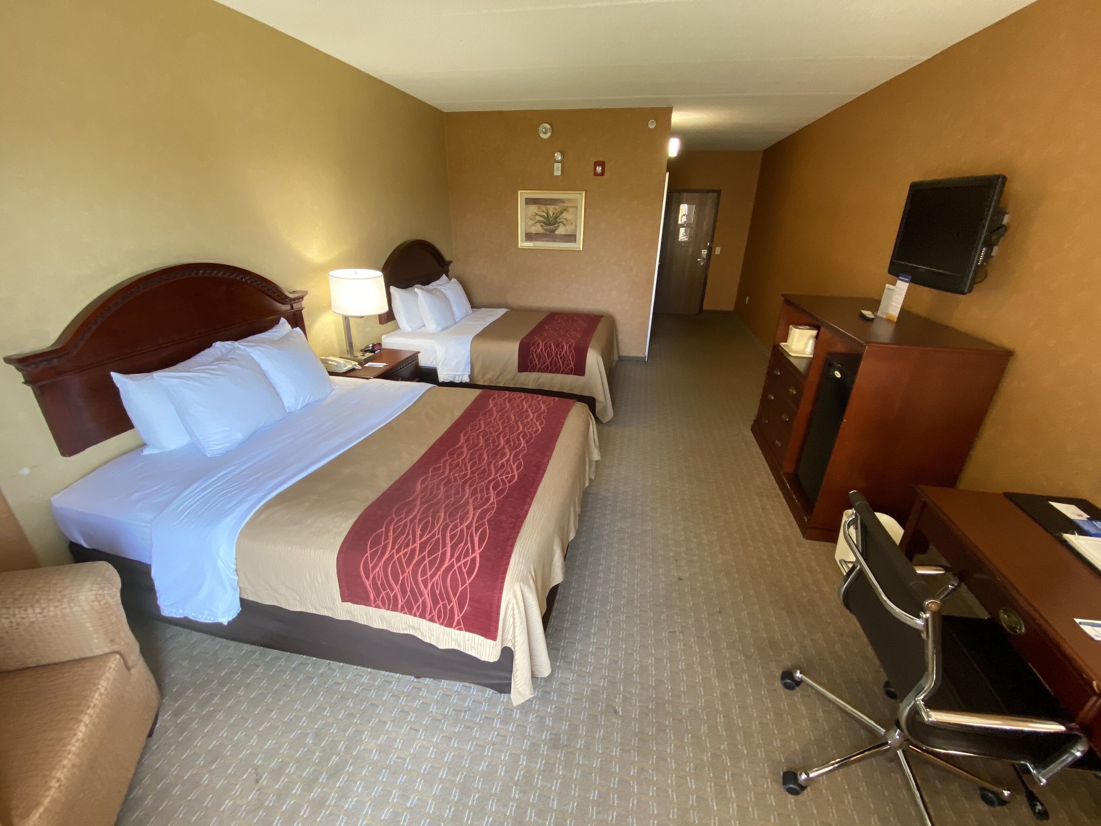 A hotel room with two beds, a desk, a chair, a television, and a door leading to another room.