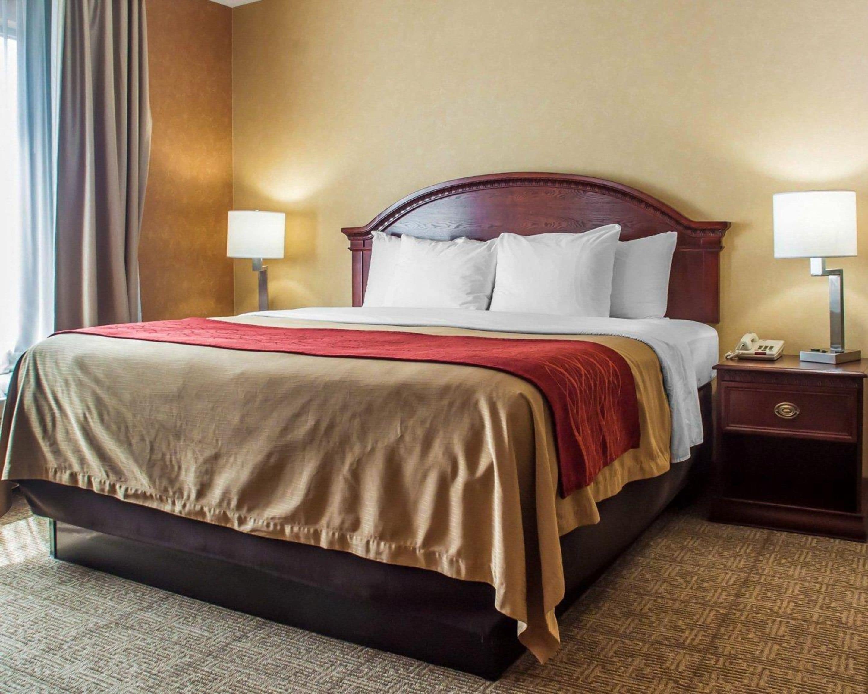 Ein Hotelzimmer mit einem großen Bett, zwei Nachttischlampen, einem Nachttisch mit Telefon und Teppichboden.