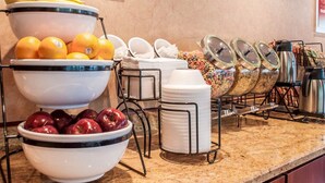 A buffet setup with bowls of fruits, cereal, and stacked plates.