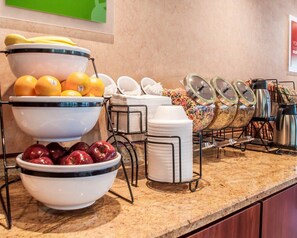 A buffet setup with bowls of fruits, cereal, and stacked plates.