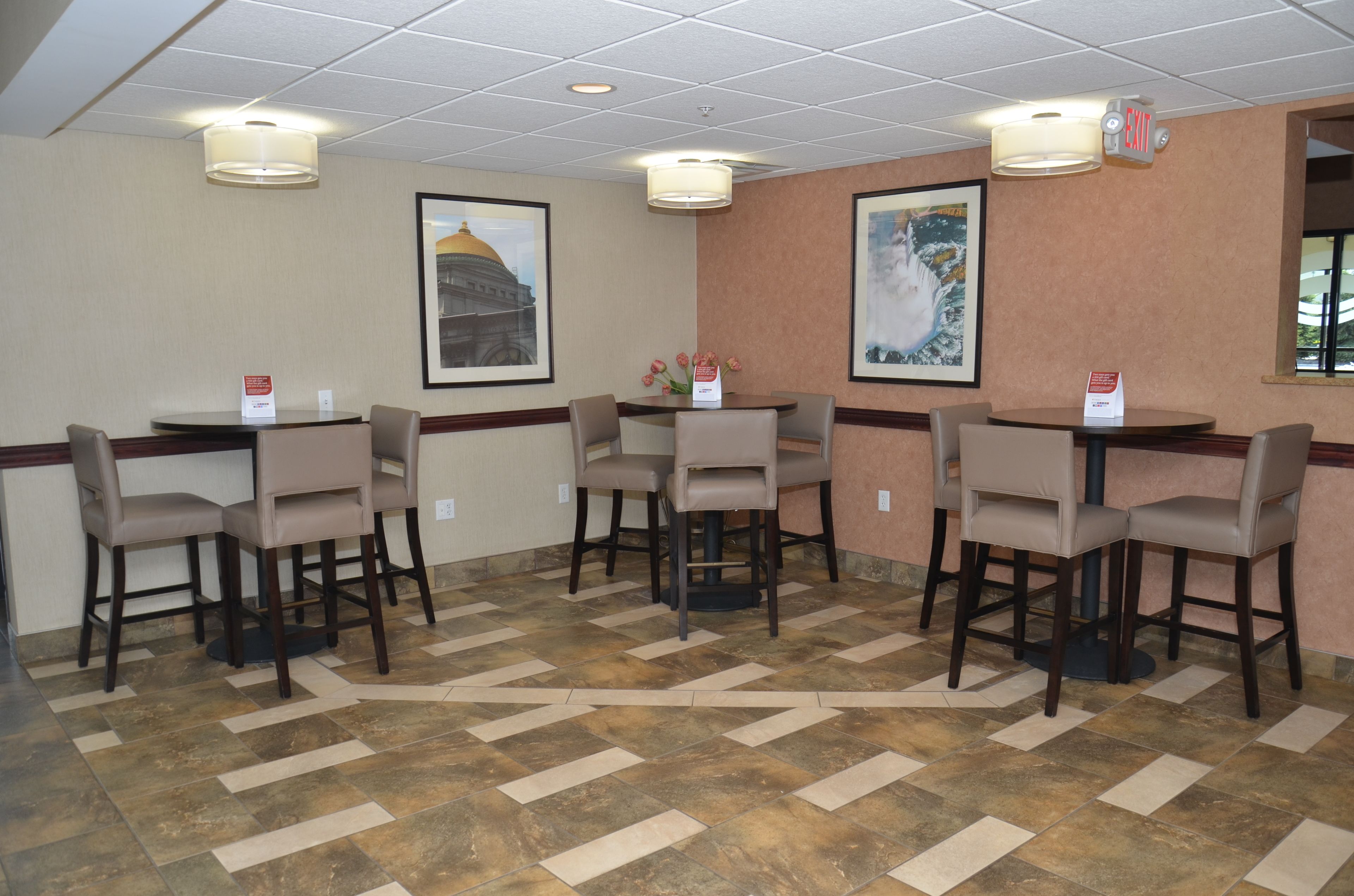 A hotel room with a tiled floor, a round table with four chairs, and two framed pictures on the wall.