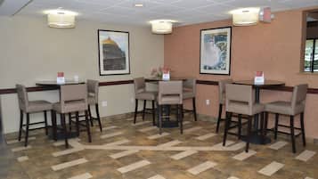 A hotel room with a tiled floor, a round table with four chairs, and two framed pictures on the wall.