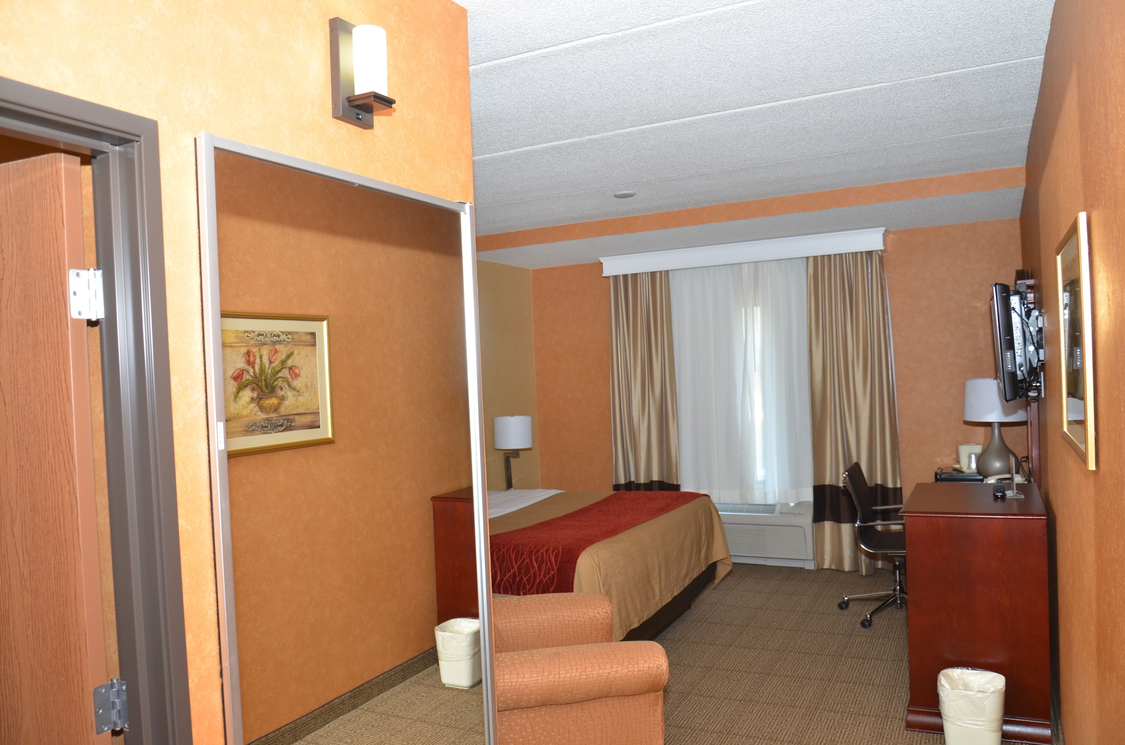 A hotel room with a bed, a desk, a chair, a trash bin, and a painting on the wall.