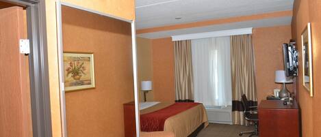 A hotel room with a bed, a desk, a chair, a trash bin, and a painting on the wall.