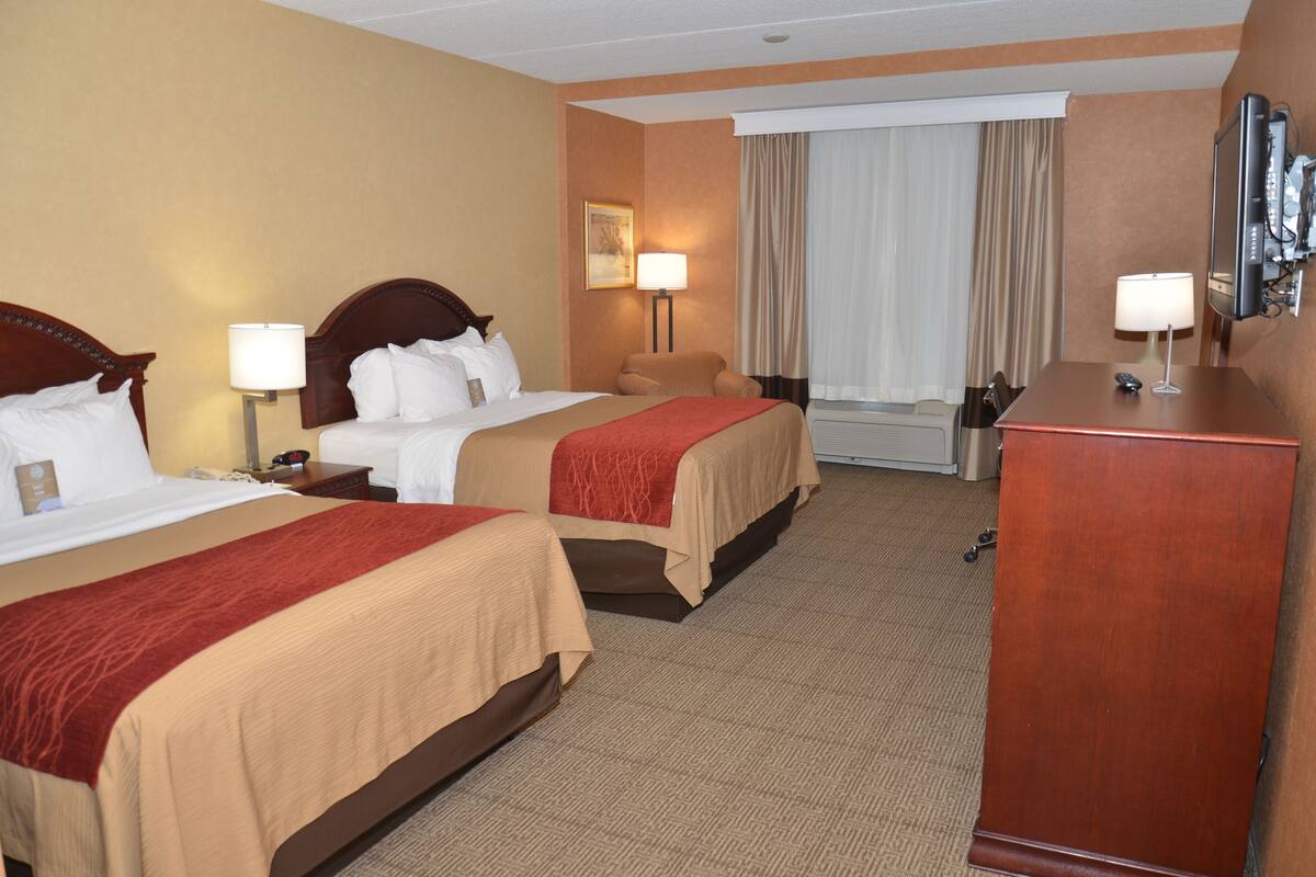 A hotel room with two beds, a desk, a chair, a TV, and a window with curtains.