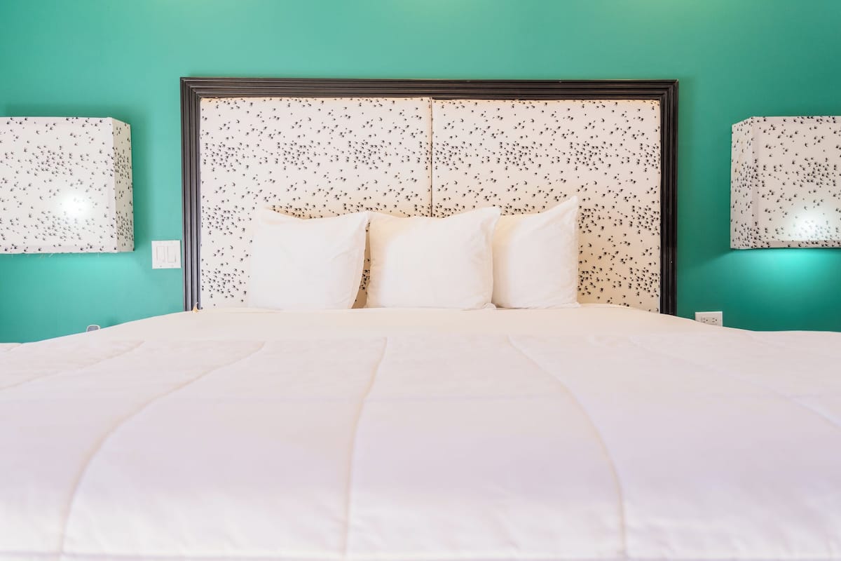 Una cama con ropa de cama blanca, cabecera con estampado moteado y dos lámparas fijadas a la pared.
