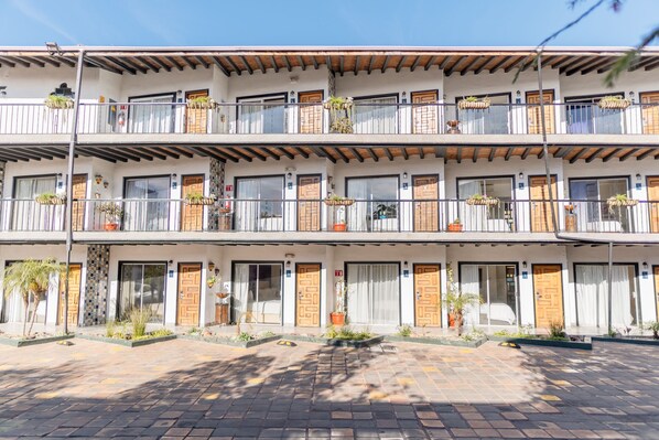 A multi-story hotel with balconies, potted plants, and a paved entrance area. - Posada El Rey Sol (Ensenada)