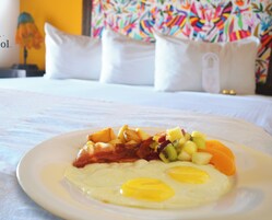 Un plato de desayuno con huevos, tocino y fruta sobre una cama en una habitación de hotel.