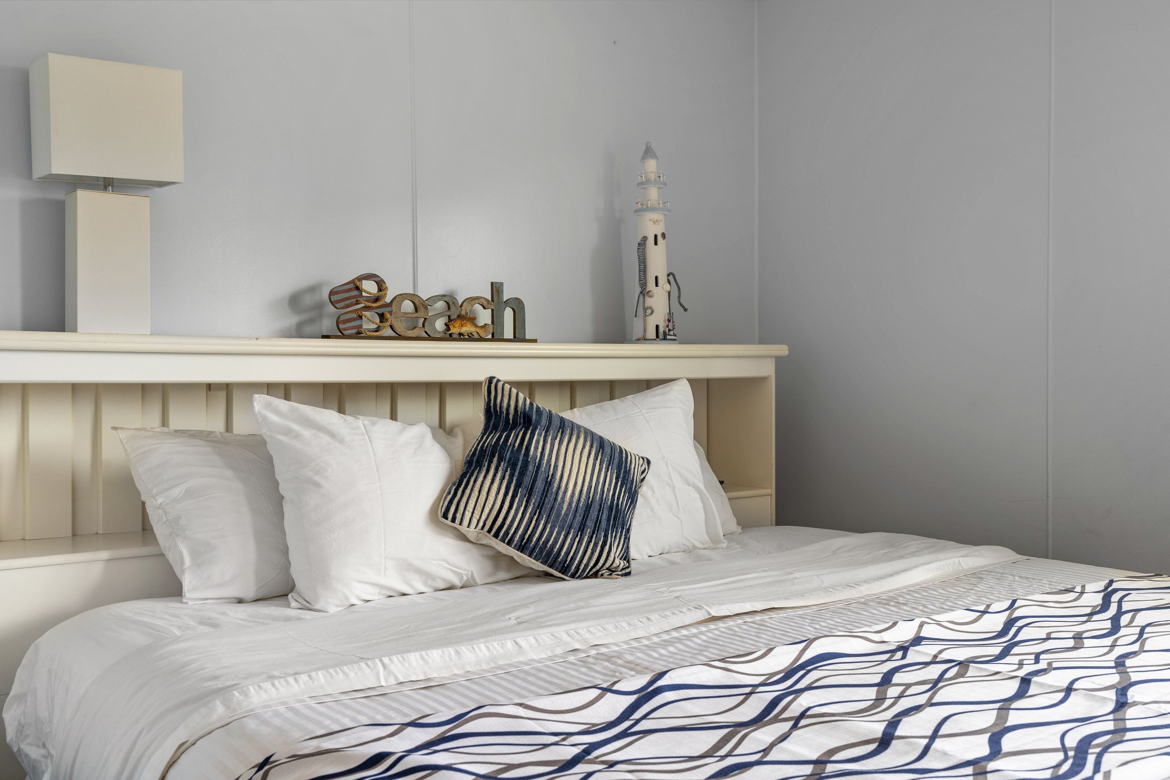 A neatly made bed with white bedding and a blue and white patterned throw.