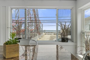 Una habitación con un ventanal que da a una zona de construcción, una silla blanca y una maceta de madera con una planta.