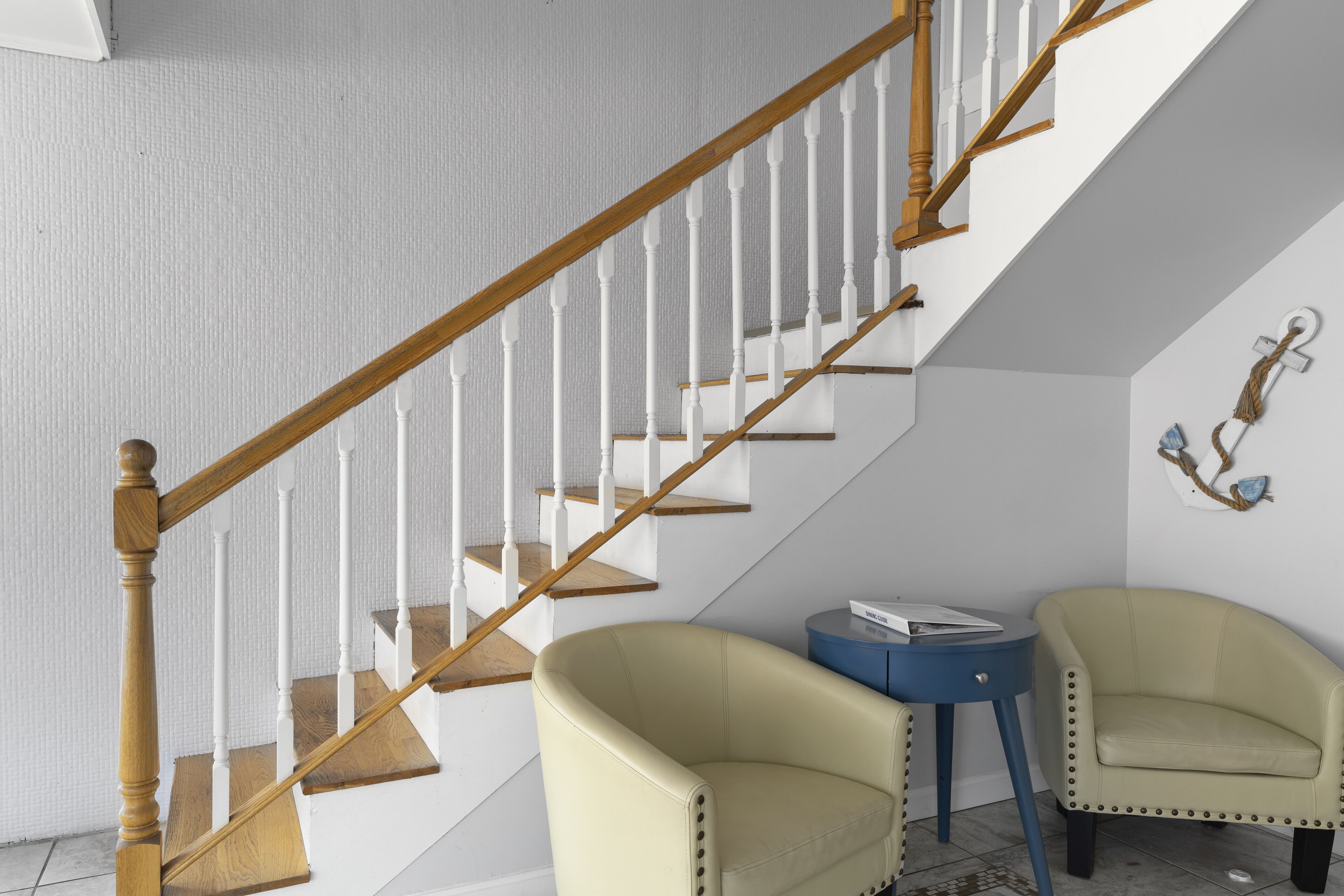 A staircase with wooden balusters and white railings, a beige armchair, a blue side table, and a small decorative wall piece.