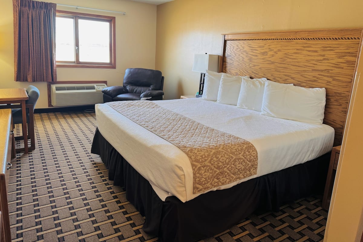 A hotel room with a large bed, a desk, a chair, and a window with curtains.