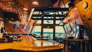 A bar with a wooden counter, hanging glasses, and a clock on the wall. - Wrangler Inn  (Mobridge)