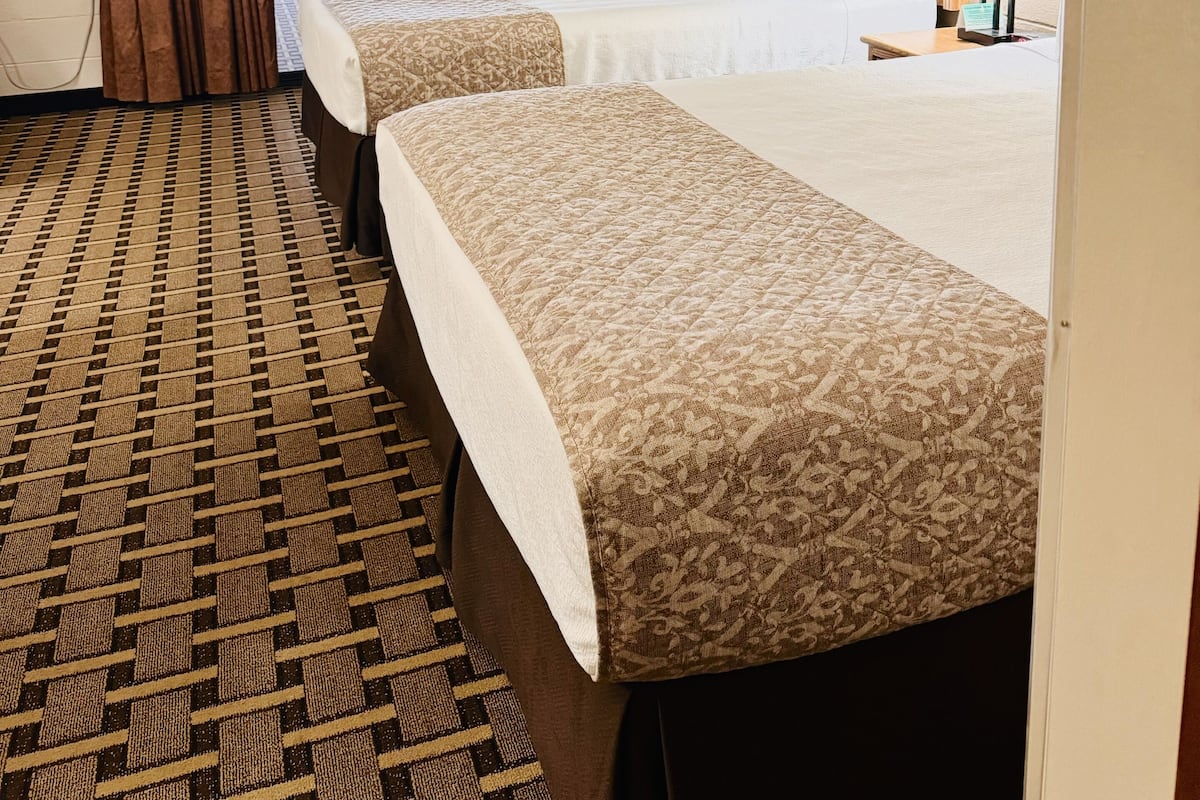 A hotel room with two beds, a large window with curtains, a view of the pool, and a small table with a lamp.