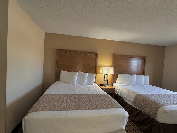 Habitación de hotel con dos camas individuales, cada una con cabecero de madera, mesita de noche con lámpara y colcha estampada.