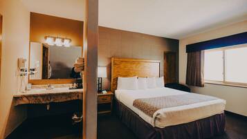 A hotel room with a large bed, a wooden headboard, a vanity with a mirror, and a window with curtains.