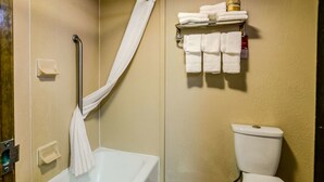 Un baño con bañera, inodoro, cortina de ducha y repisa con toallas dobladas.