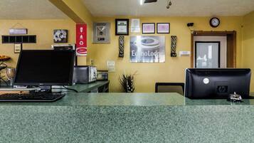 A reception desk with two monitors, a keyboard, and a telephone. There are framed certificates and a clock on the wall.