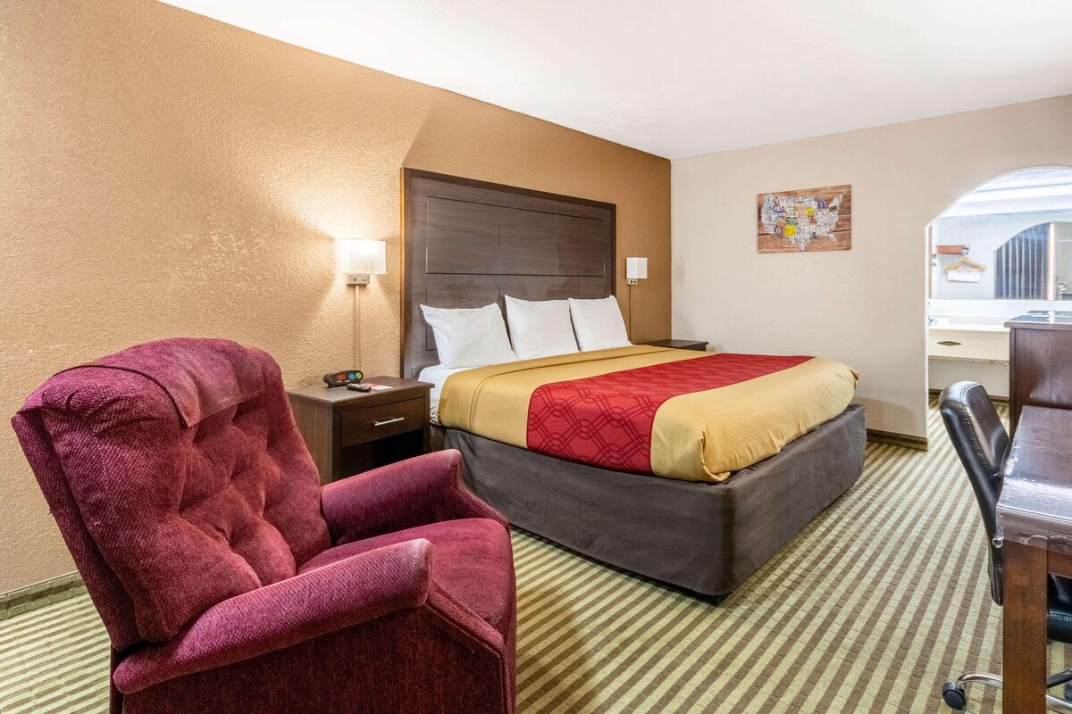 A hotel room with a large bed, a red armchair, a desk, and a map on the wall.