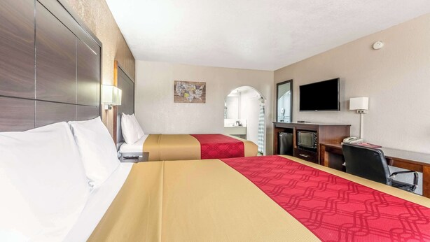 Habitación de hotel con dos camas, un escritorio, un televisor y un baño pequeño.