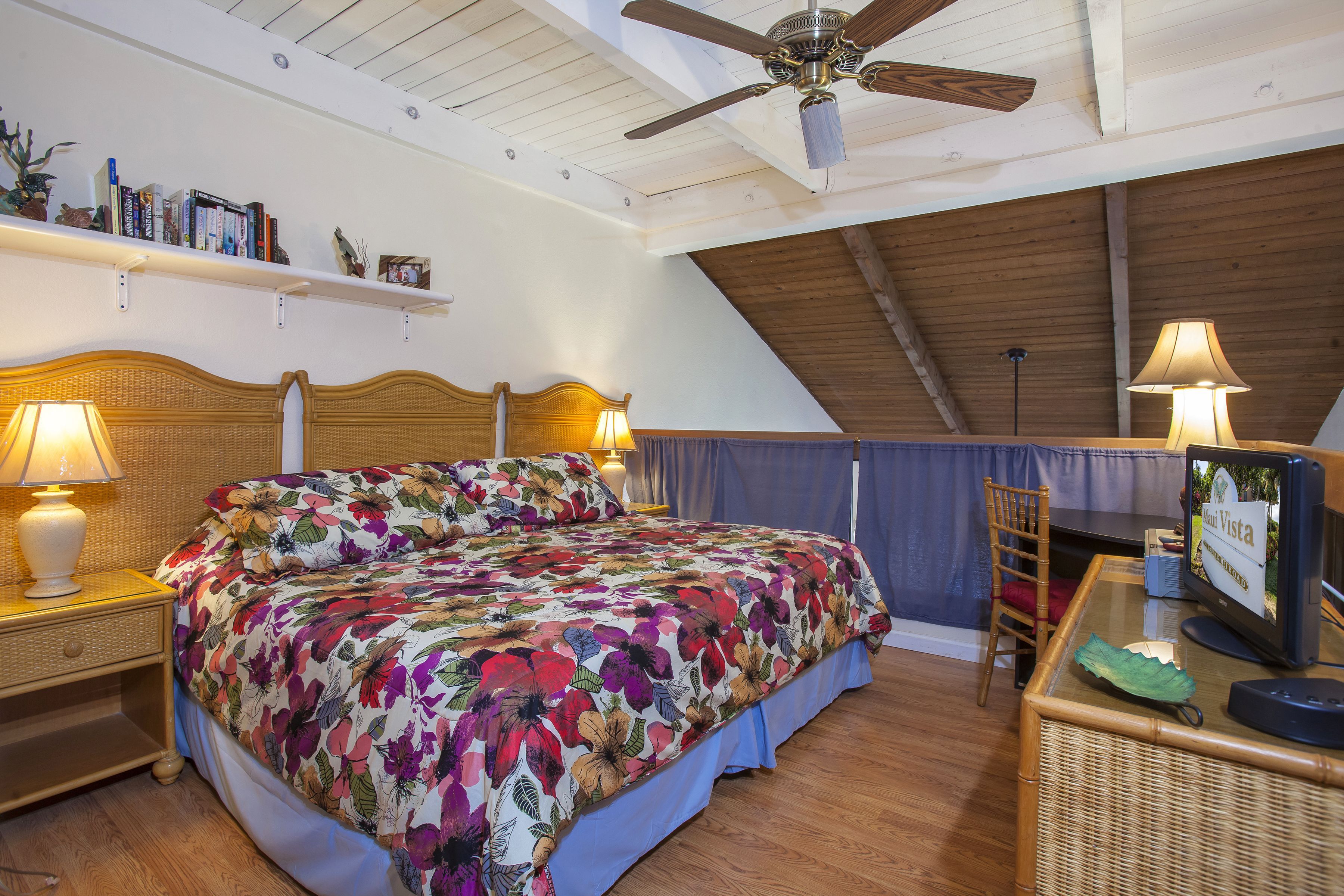 A bedroom with a bed, two bedside tables with lamps, a ceiling fan, a desk with a computer, and a chair.