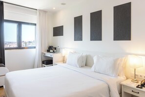 A hotel room with a large bed, a desk with a coffee machine, a lamp, and a view of the city through a window. - Hotel AS Lisboa (Lisbon)