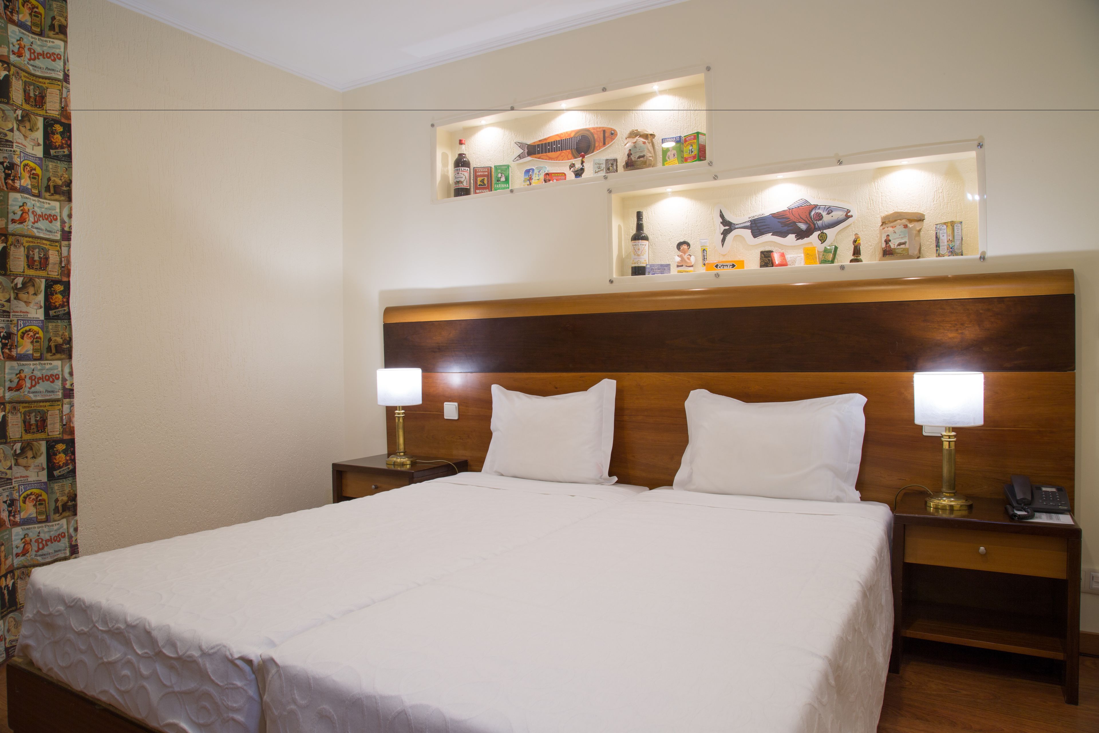 Hotelkamer met een groot bed, twee nachtkastjes met lampen, een houten hoofdeinde, en een muur met ingelijste foto's en een plank met diverse spullen.