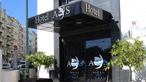 La entrada del Hotel A.S., con un letrero visible, un cartel con un mapa y algunos árboles.