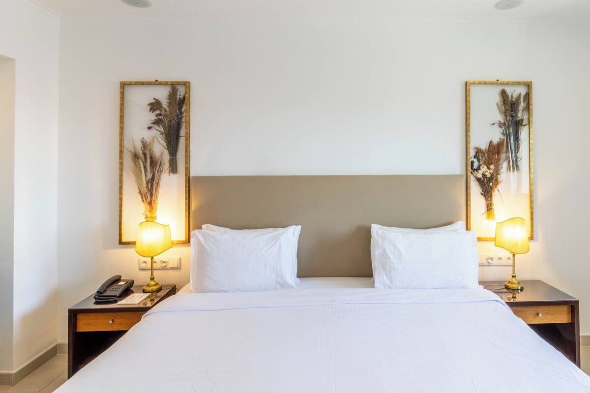 A hotel room with a large bed, two bedside tables with lamps, and framed floral artwork on the walls.