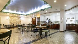 Un amplio comedor interior con suelo de baldosas, varias mesas y sillas, una zona de cocina con mostrador y un techo decorativo.