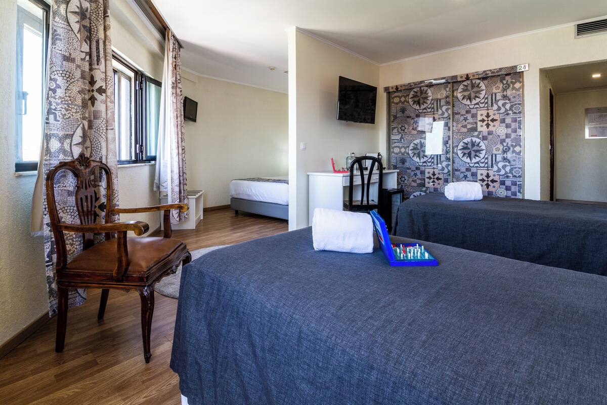 A hotel room with two beds, a desk, a chair, and a TV on the wall.