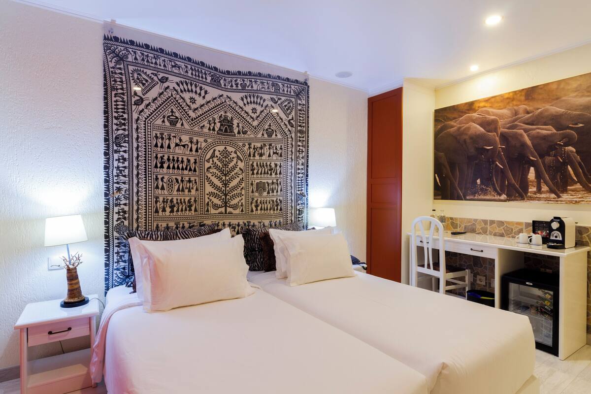 A hotel room with a bed, bedside tables, a desk, and a tapestry on the wall.