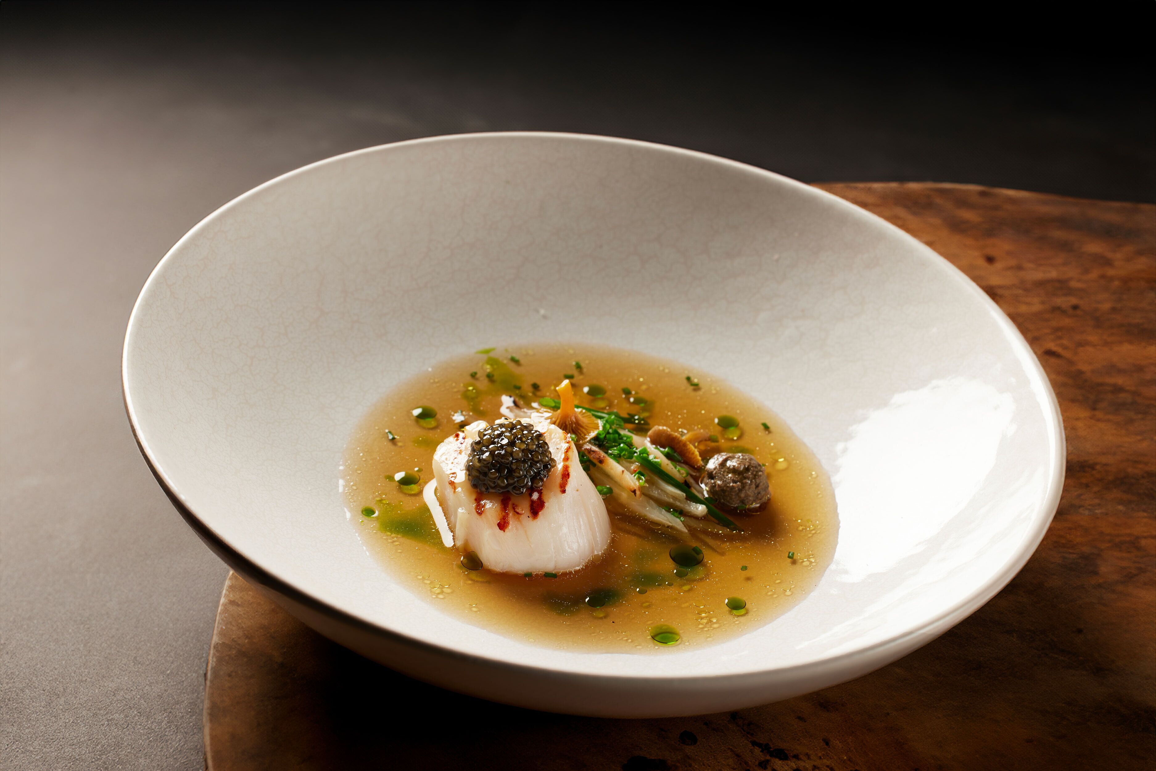 A bowl of soup with a dumpling and green garnish on a wooden table.