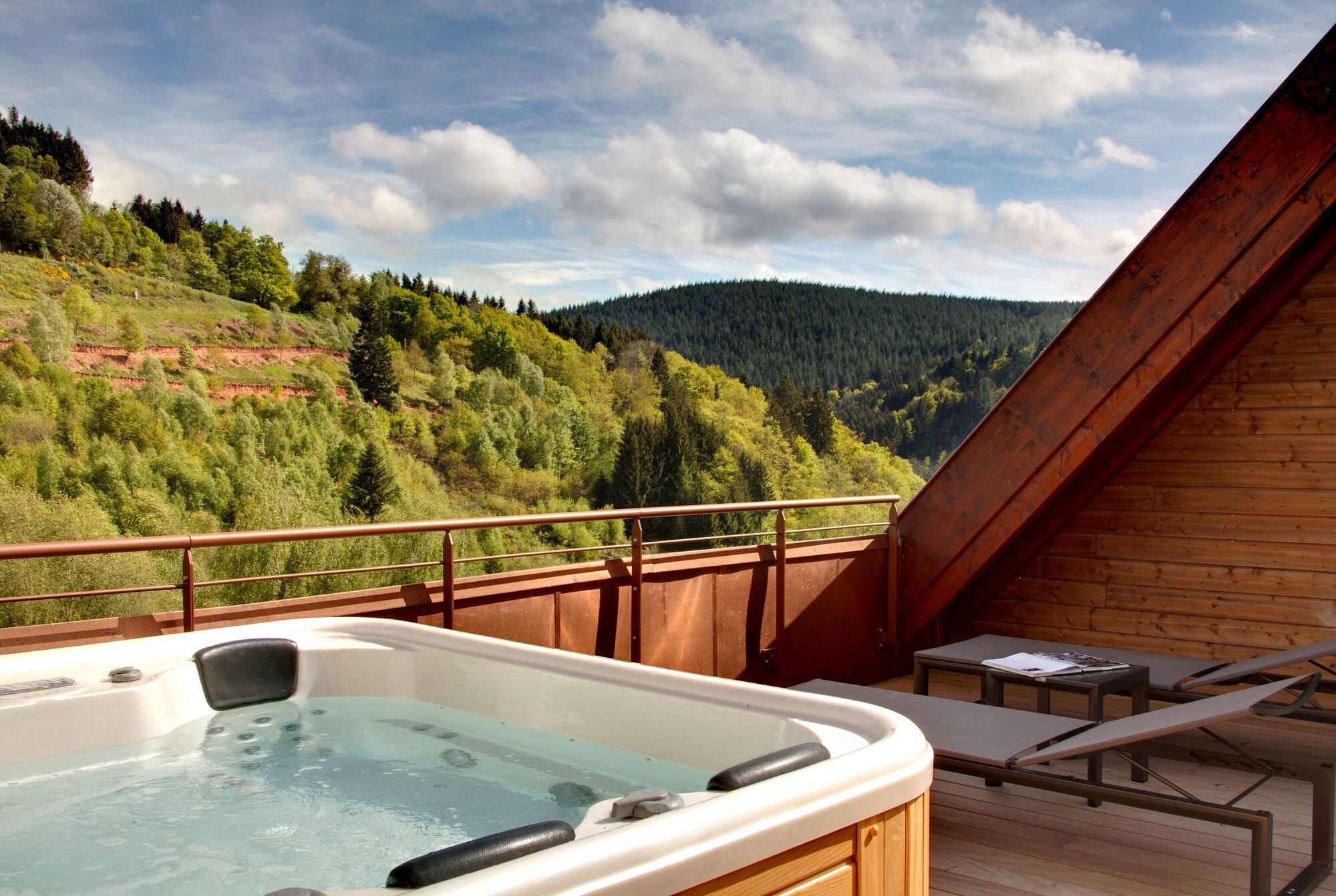 A hot tub on a wooden deck with a view of a forested hillside.