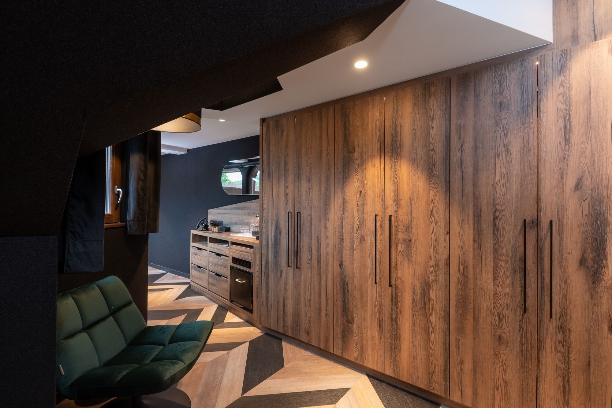 A modern interior with a wooden wardrobe, a green sofa, and a kitchen area.
