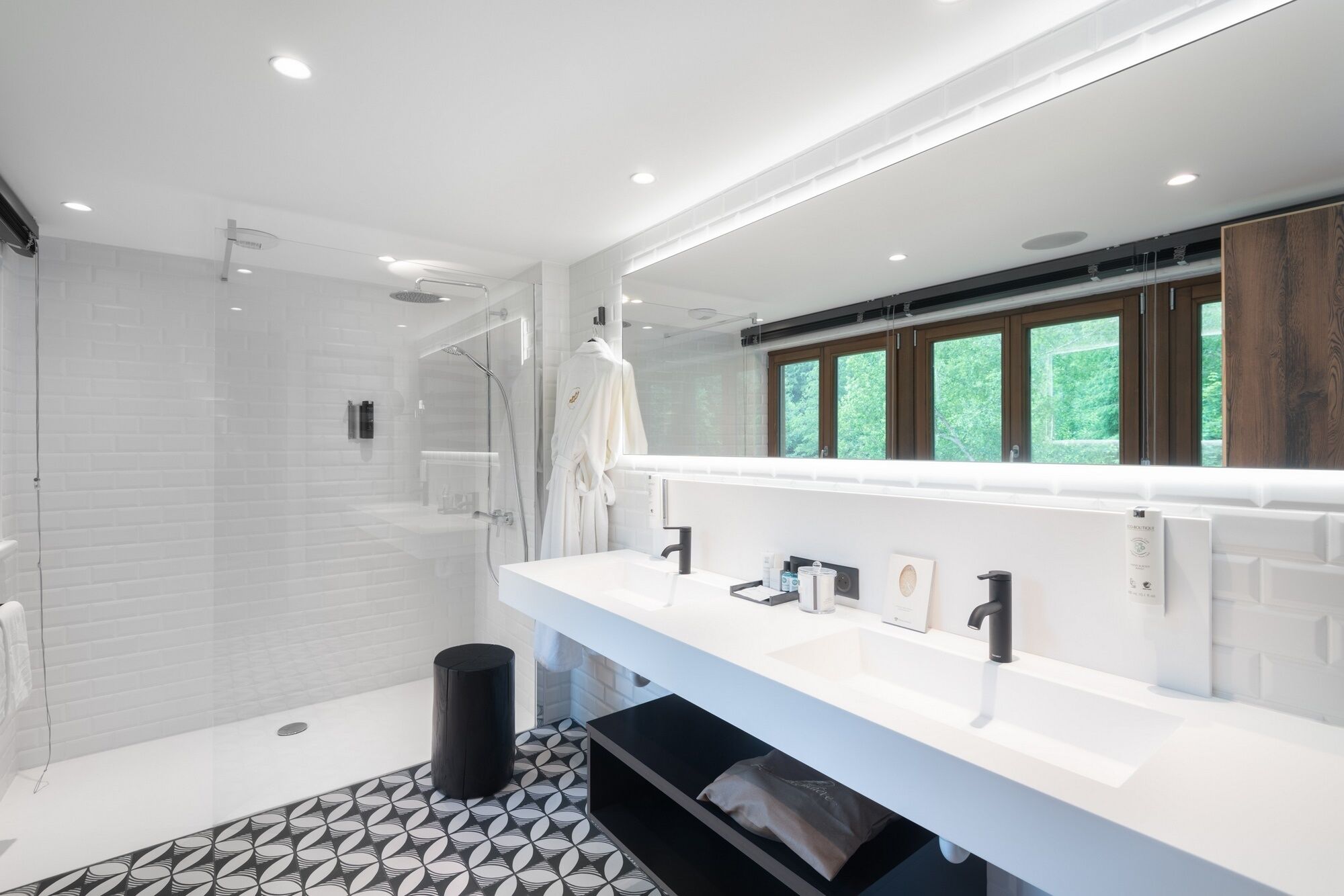 Een moderne badkamer met een douchecabine van glas, een grote spiegel en een wit wastafelmeubel met twee wasbakken.
