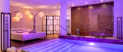 A modern spa area with a large pool, a massage room, and a wall with a textured pattern.