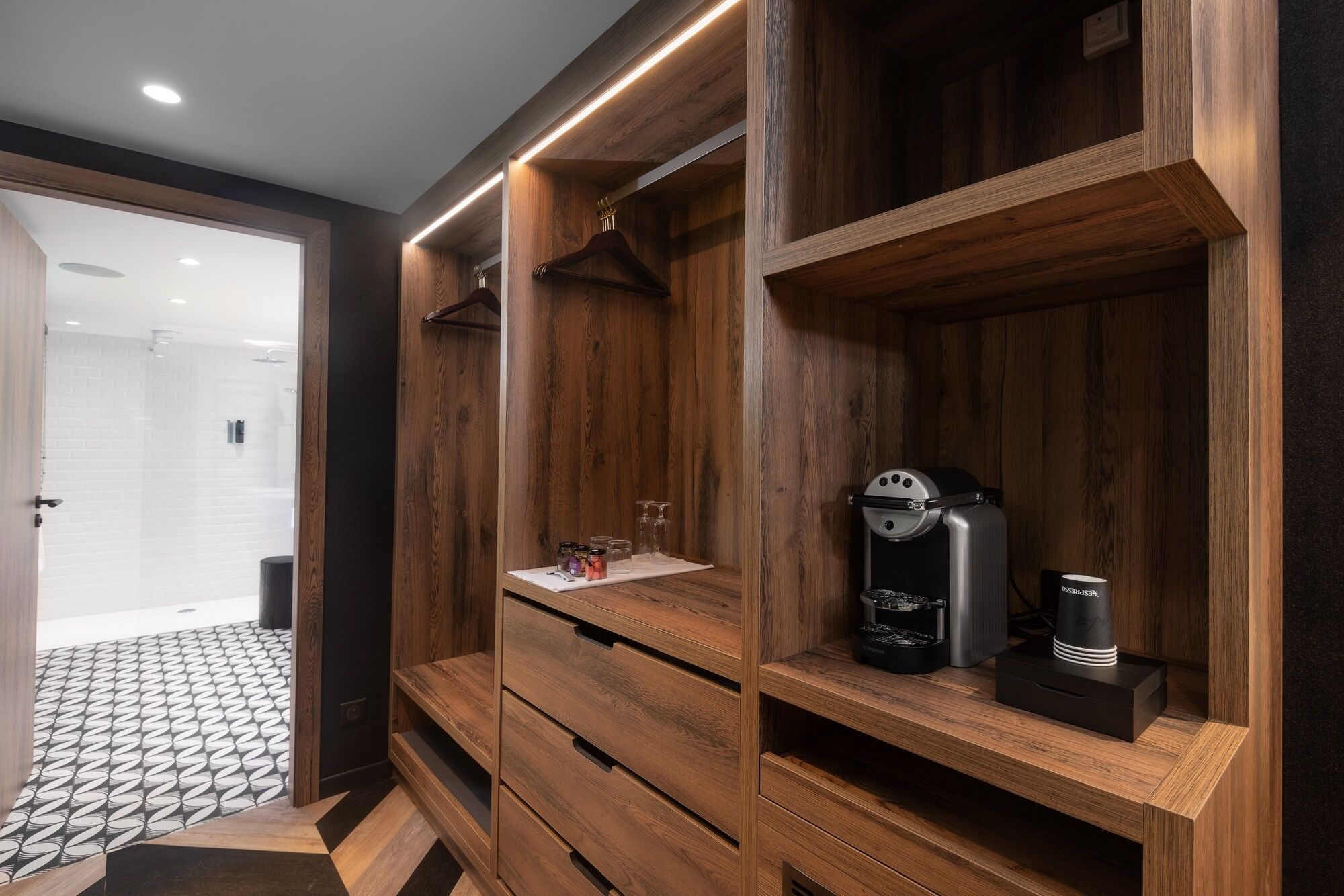 A modern bathroom with wooden cabinetry, a coffee machine, and a glass shower enclosure.