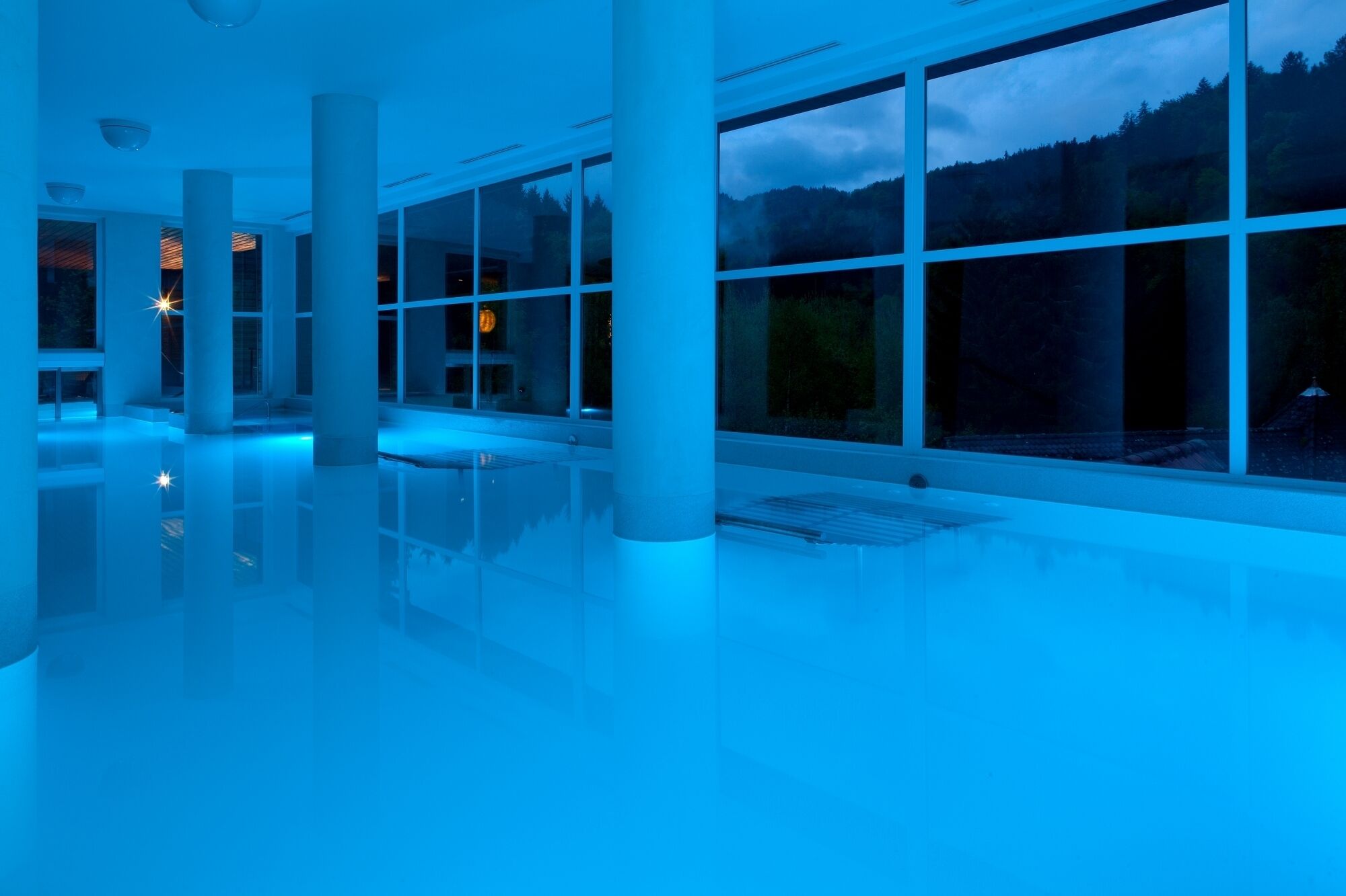 Un amplio espacio interior con grandes ventanales y una iluminación azulada.