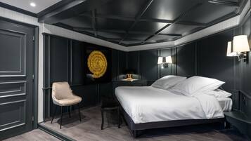 Ein modernes Schlafzimmer mit einem großen Bett, einem Sessel, einem Schreibtisch und einer dekorativen Wandgestalt.